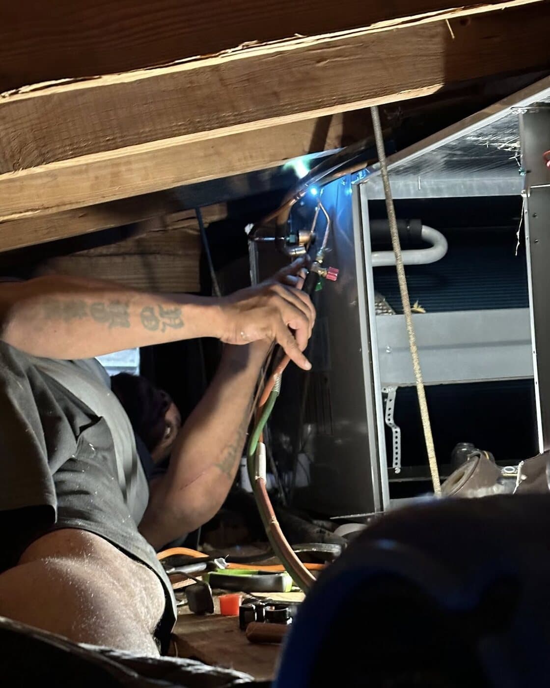 Quel Moragne in a floor crawlspace, brazing a refrigerant line at the air handler by torchlight.